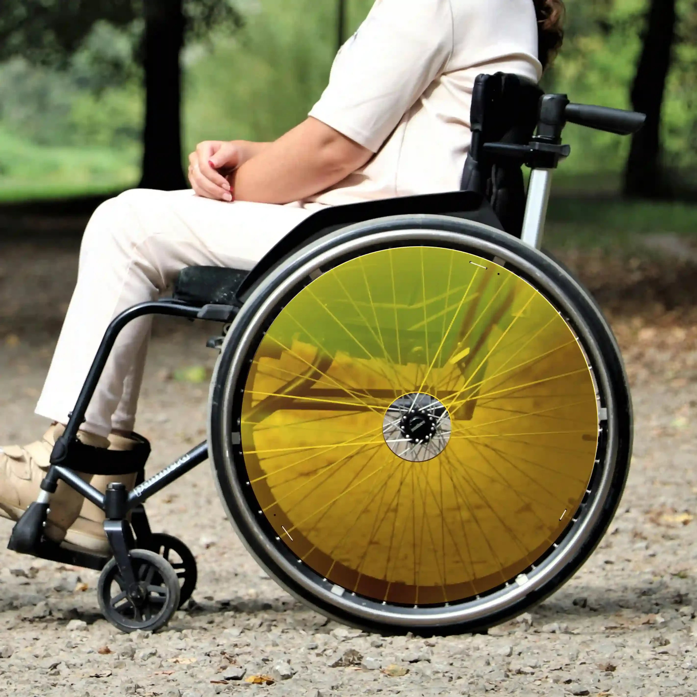 Woman in wheelchair with yellow spoke guards outdoors, showcasing wheelchair accessory