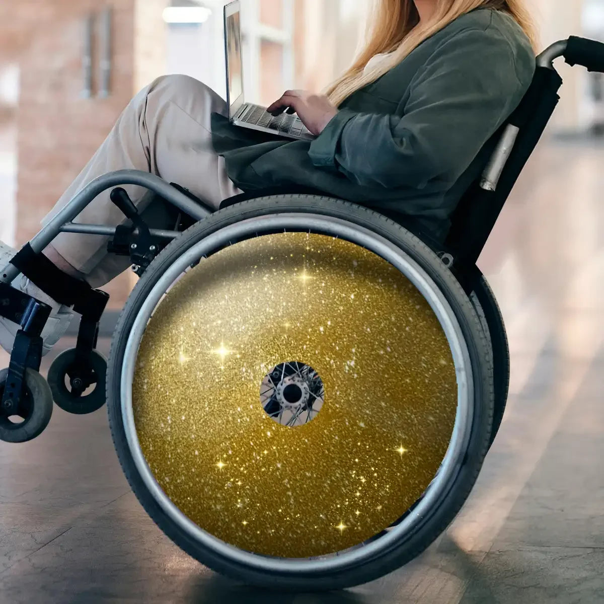 Woman using wheelchair with sparkling gold spoke guards, working on a laptop indoors