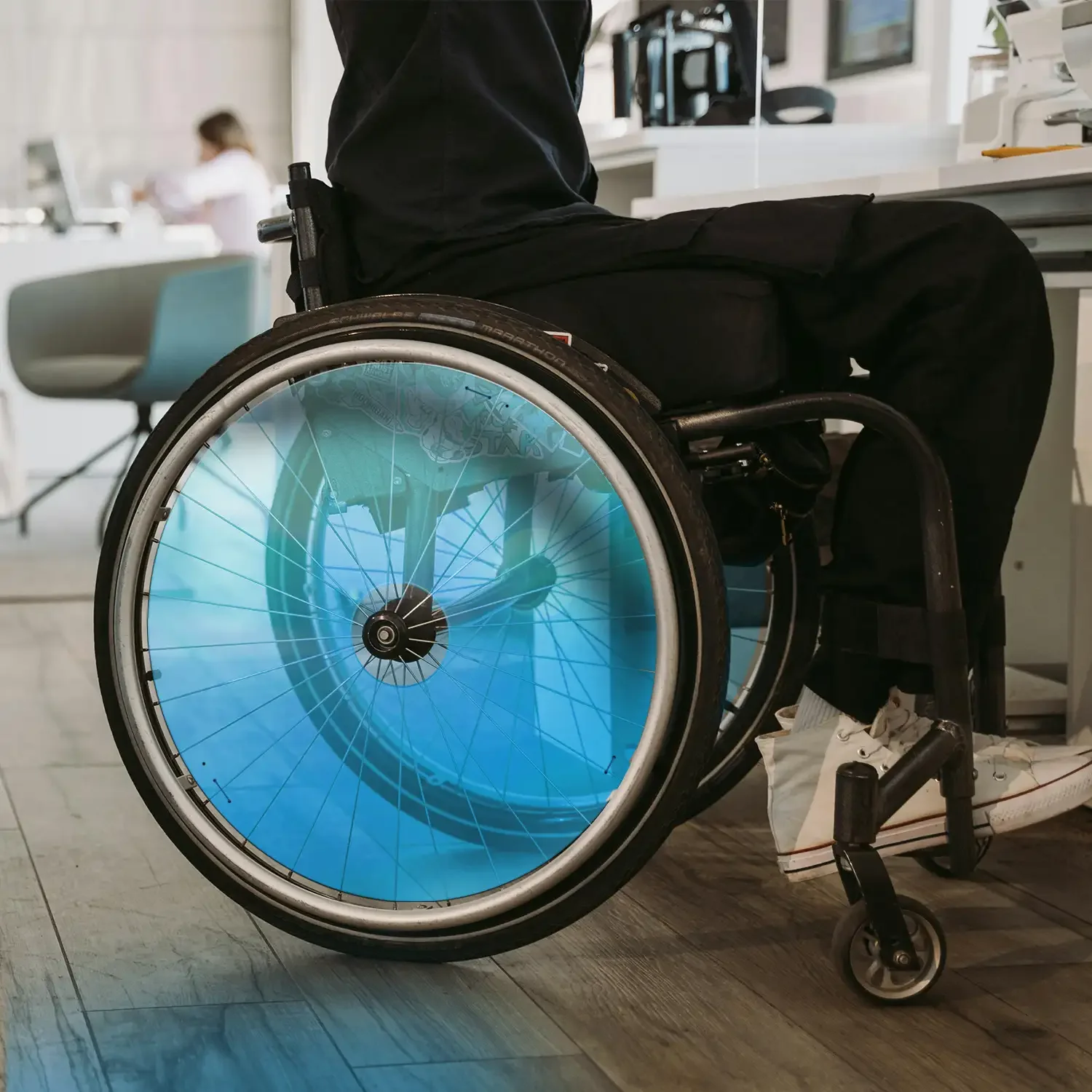 Rollstuhlnutzer im Innenbereich mit blauem Rollstuhl-Speichenschutz, moderner barrierefreier Arbeitsplatz