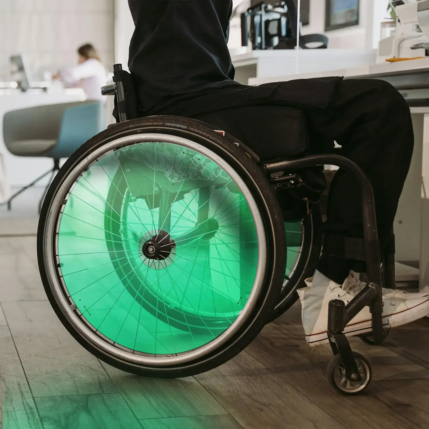 Man using wheelchair with bright green spoke guards indoors, wheelchair accessories