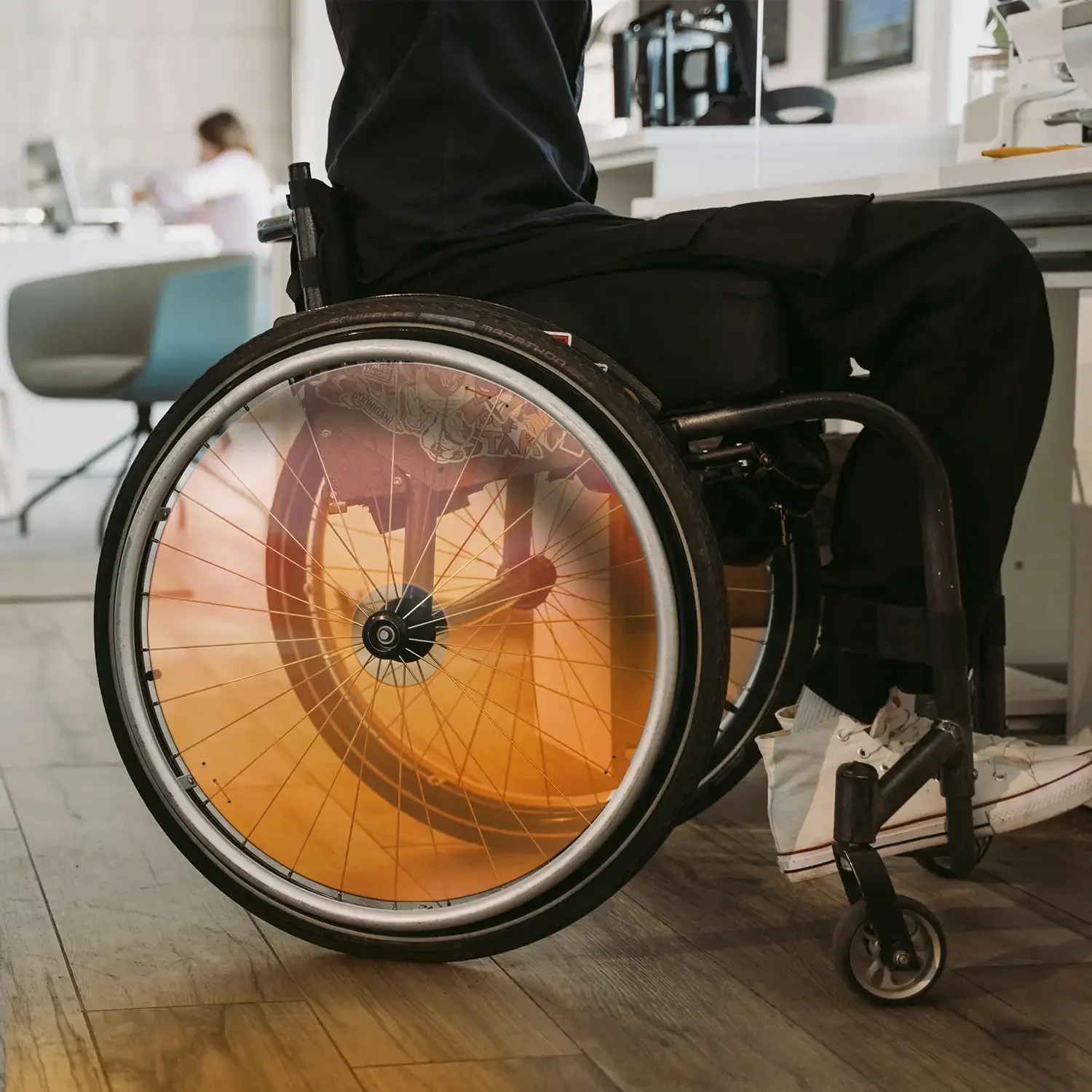 Mann im Rollstuhl mit orangefarbenem Speichenschutz sitzt im Innenbereich, mit langlebigem Rollstuhlzubehör