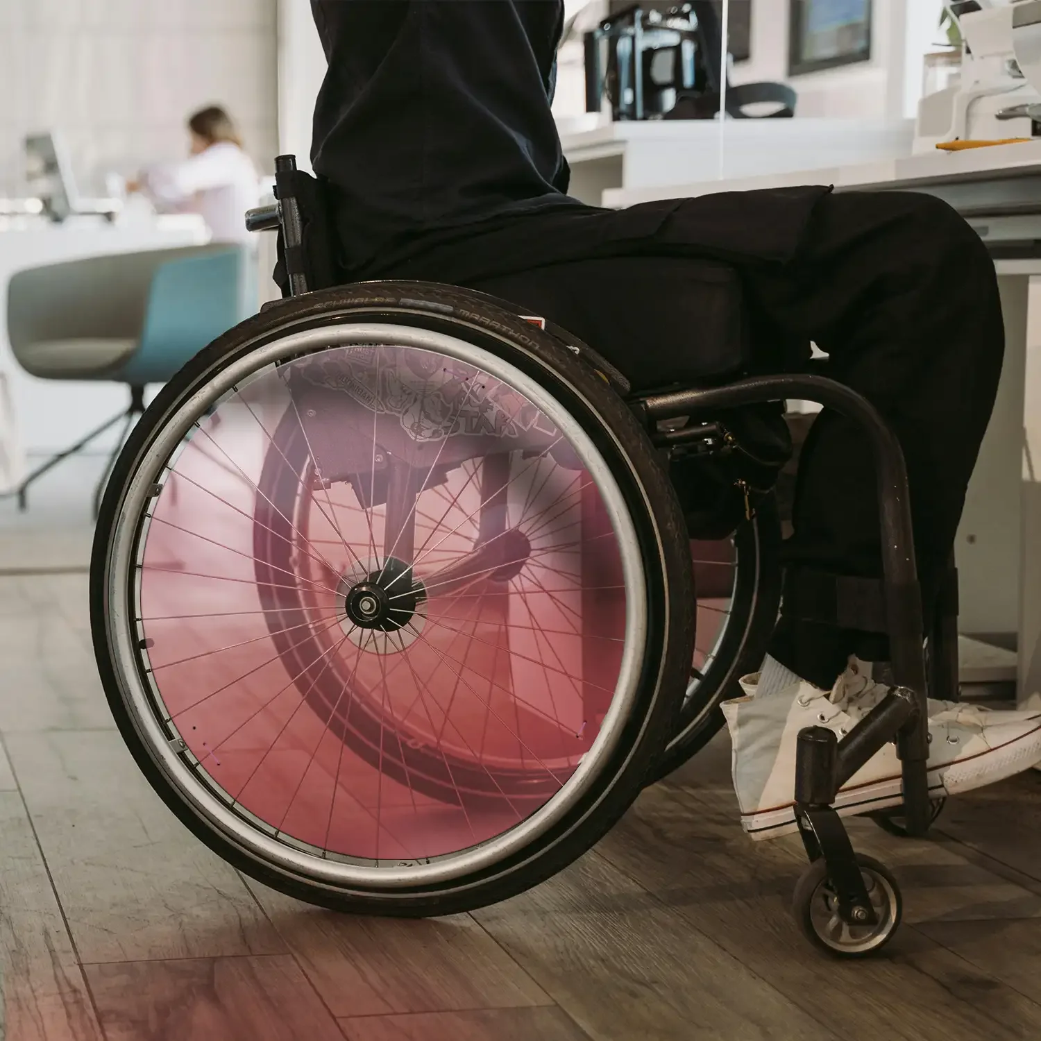 Mann sitzt im Rollstuhl mit pinkfarbenem Speichenschutz in moderner Büroumgebung