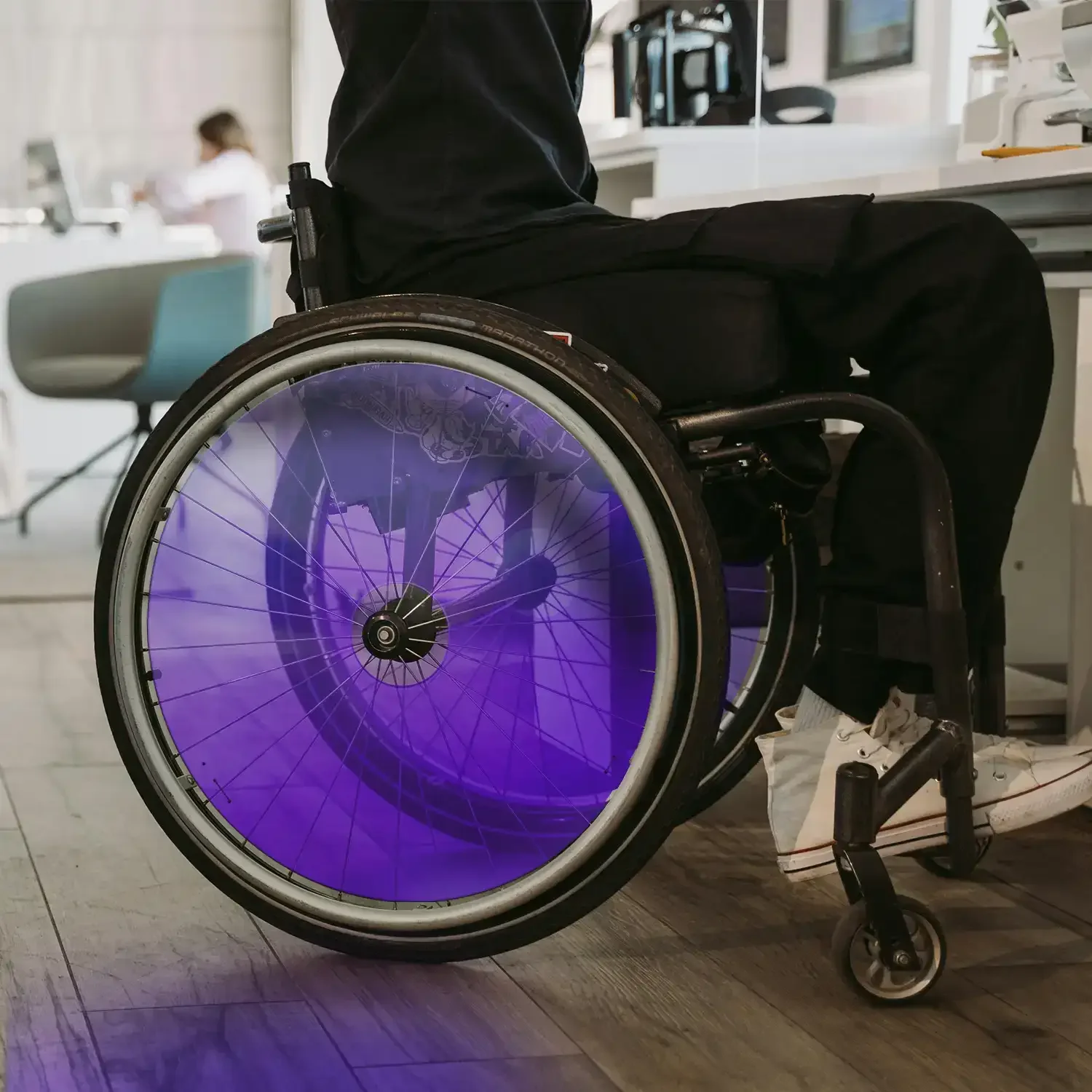 Man in wheelchair with purple spoke guards in a modern indoor setting