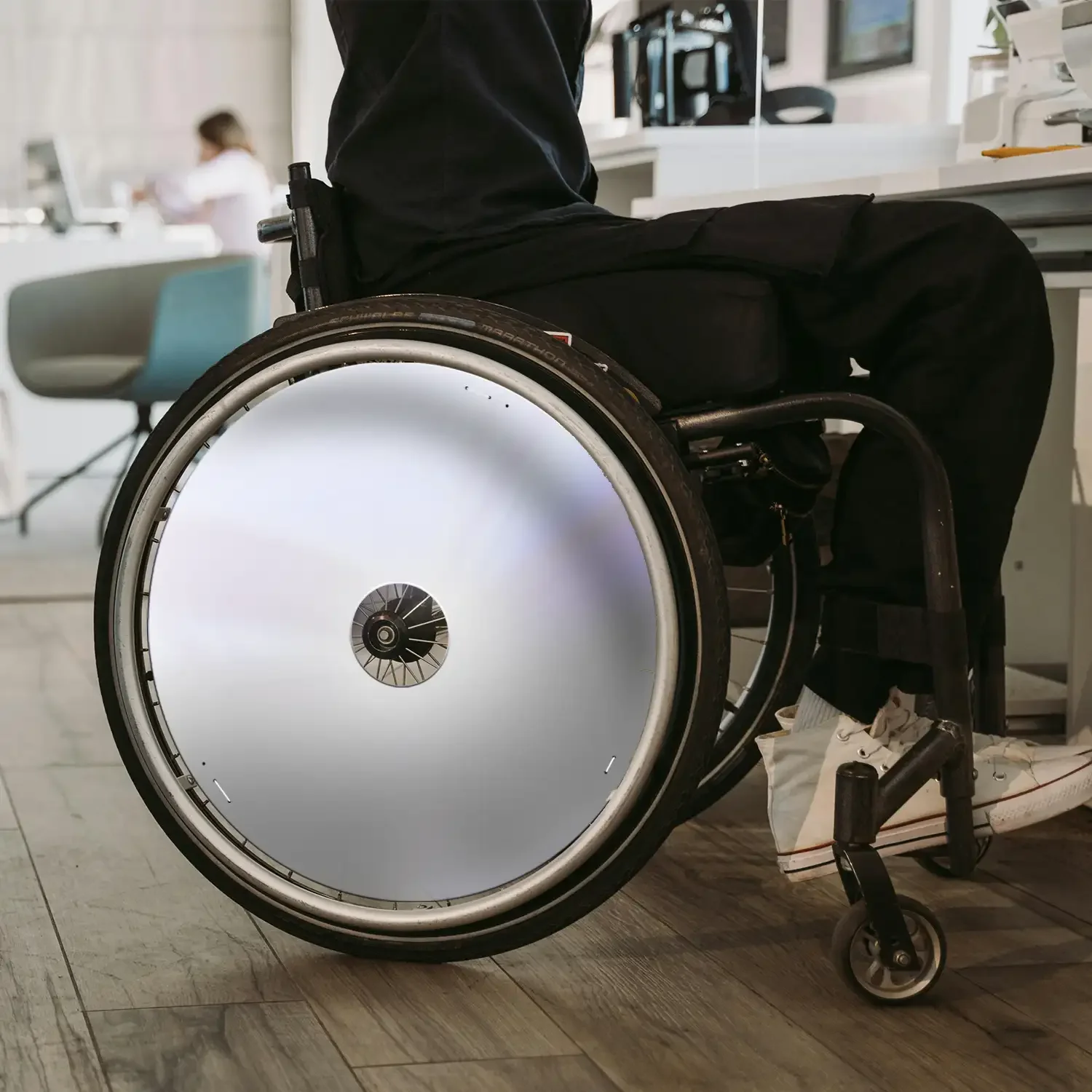 Man in rolstoel met strakke witte spaakbeschermers binnen, toont rolstoelaccessoire