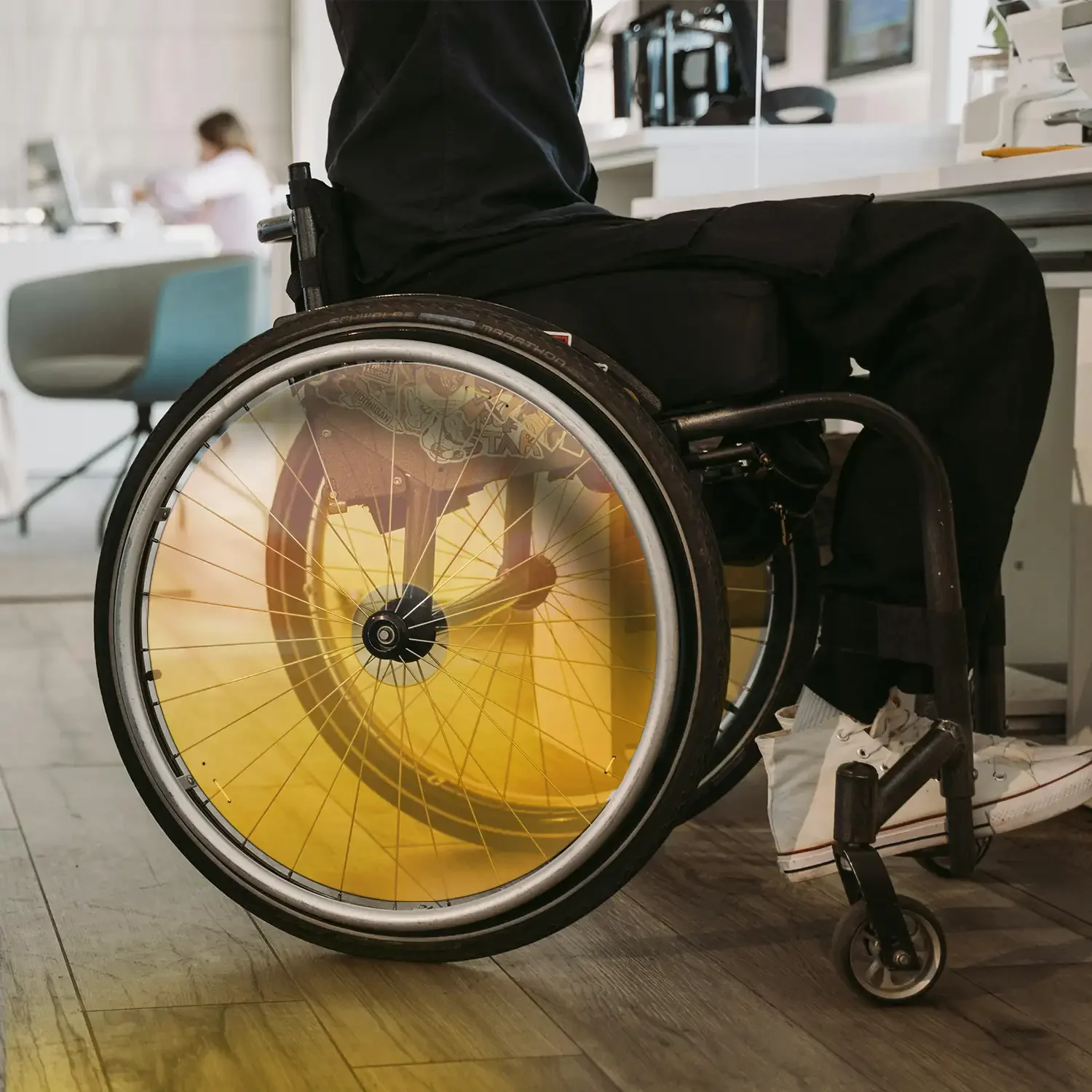 Man in wheelchair with yellow spoke guards sitting indoors on wooden floor