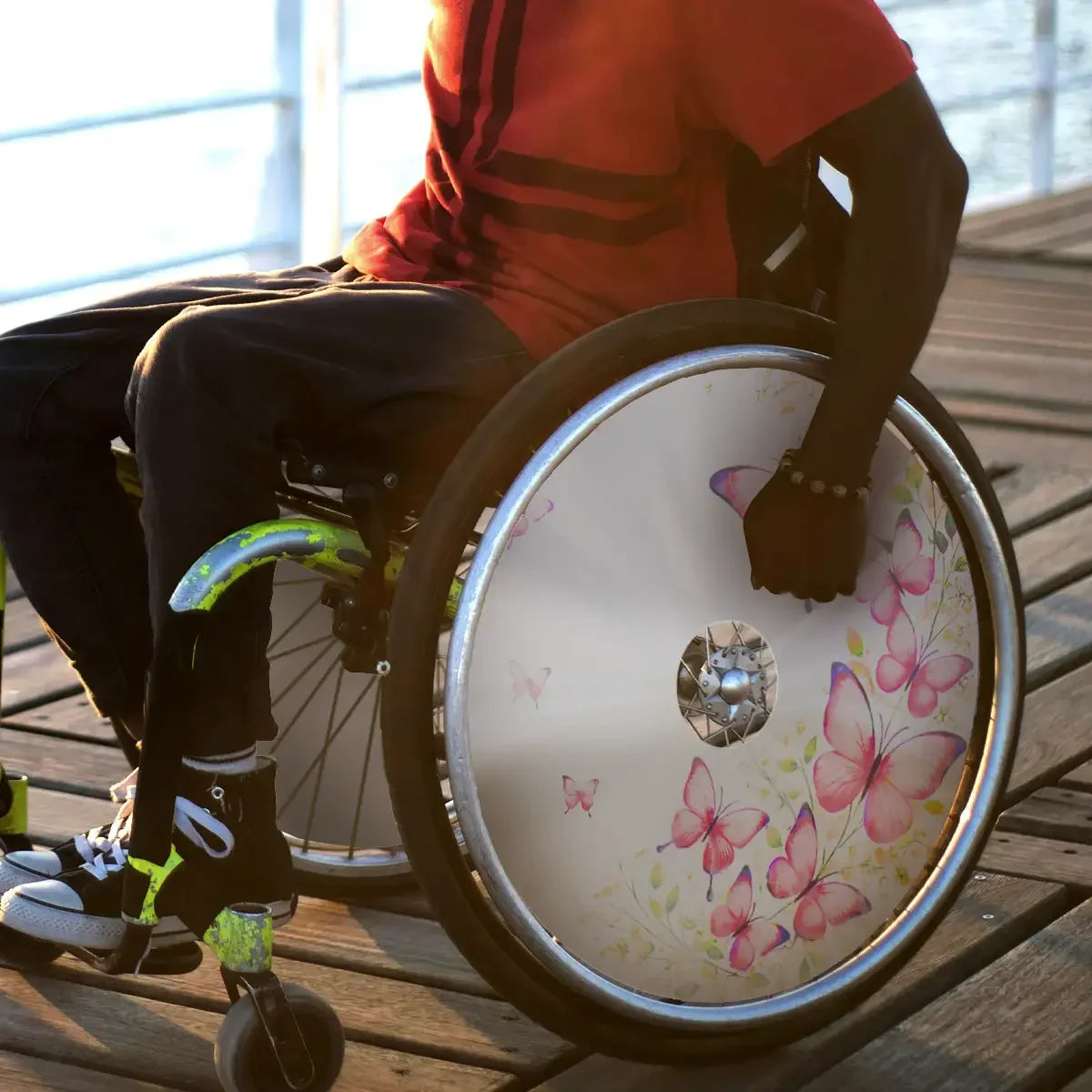 Wheelchair with butterfly spoke guard design outdoors, man in red shirt on wooden deck