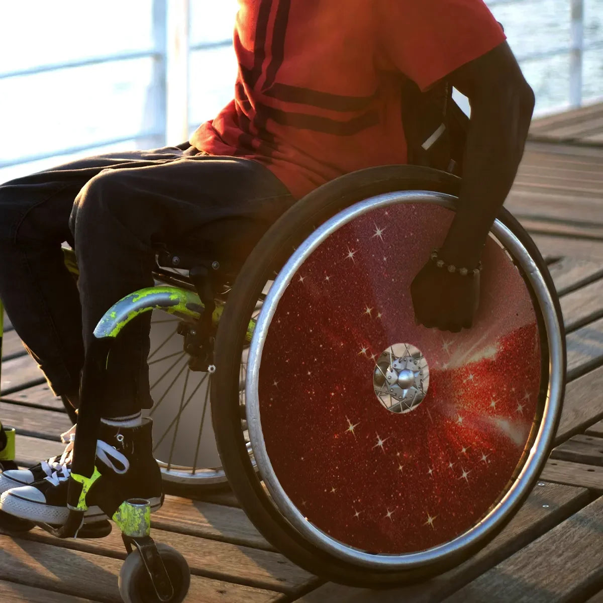Person in wheelchair with red galaxy spoke guards on wooden dock, wheelchair accessories for mobility