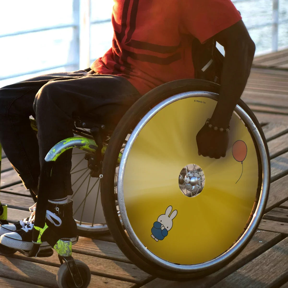 Man in wheelchair with yellow Miffy letting go balloon spoke guard on boardwalk