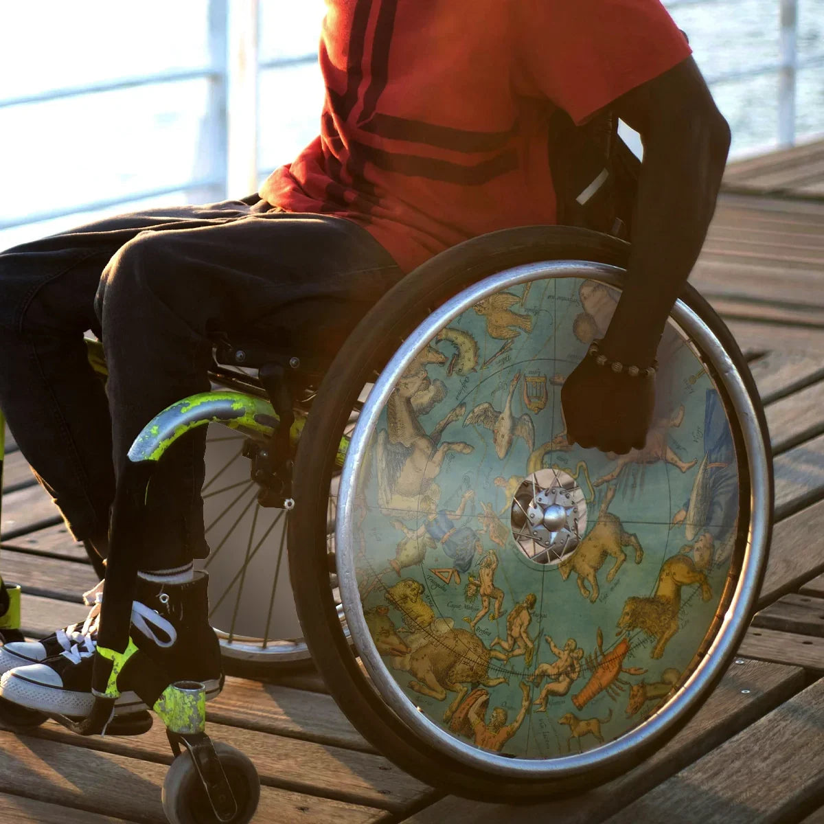Man in wheelchair with celestial globe spoke guards on wheel, outdoors on wooden deck