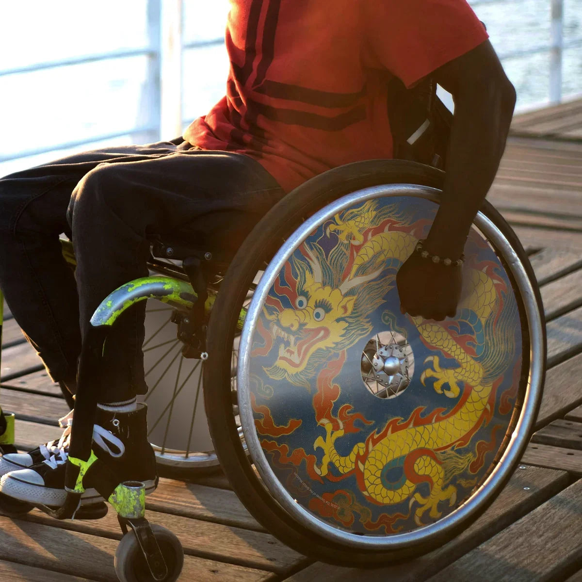 Man in wheelchair with colorful dragon spoke guard on wheel, outdoors on wooden deck
