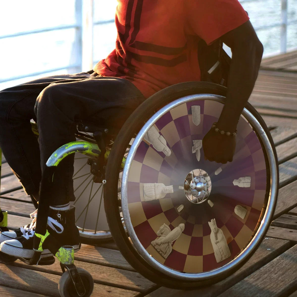 Man in wheelchair on wooden deck with chess-themed spoke guard on wheel
