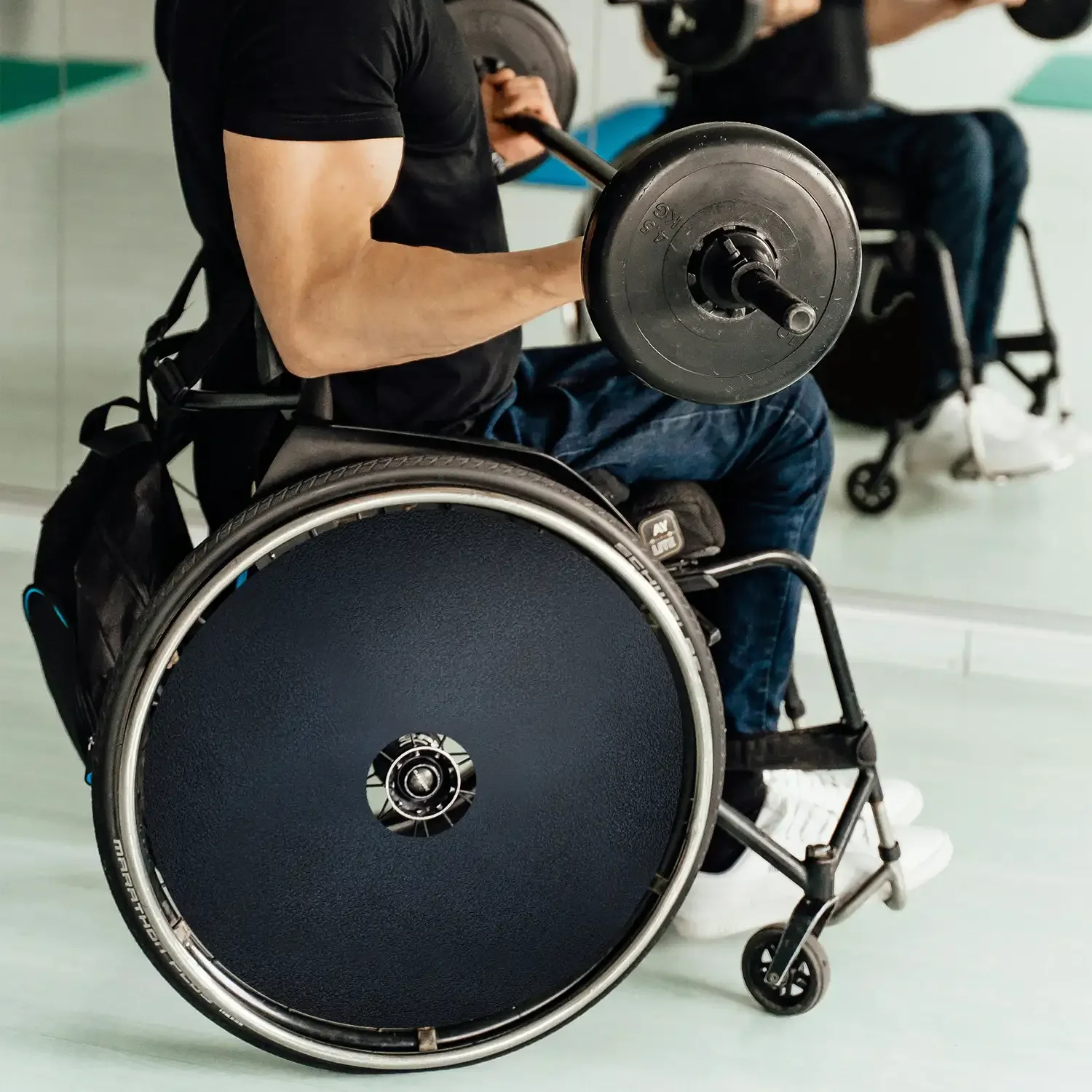 Man in wheelchair using spoke guards, lifting barbell in gym setting