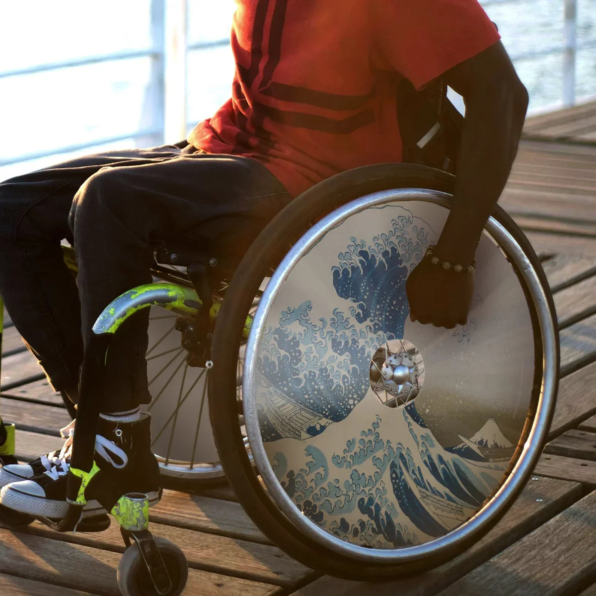 Man in wheelchair with Great Wave art spoke guards on wheel, outdoors on wooden deck