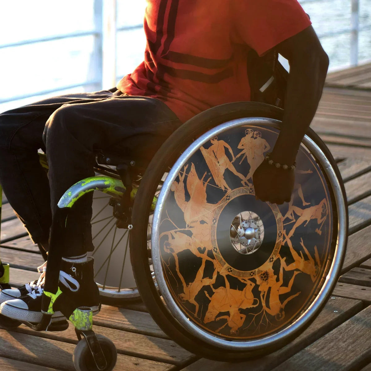 Wheelchair user on boardwalk with Greek mythology themed spoke guards on wheel