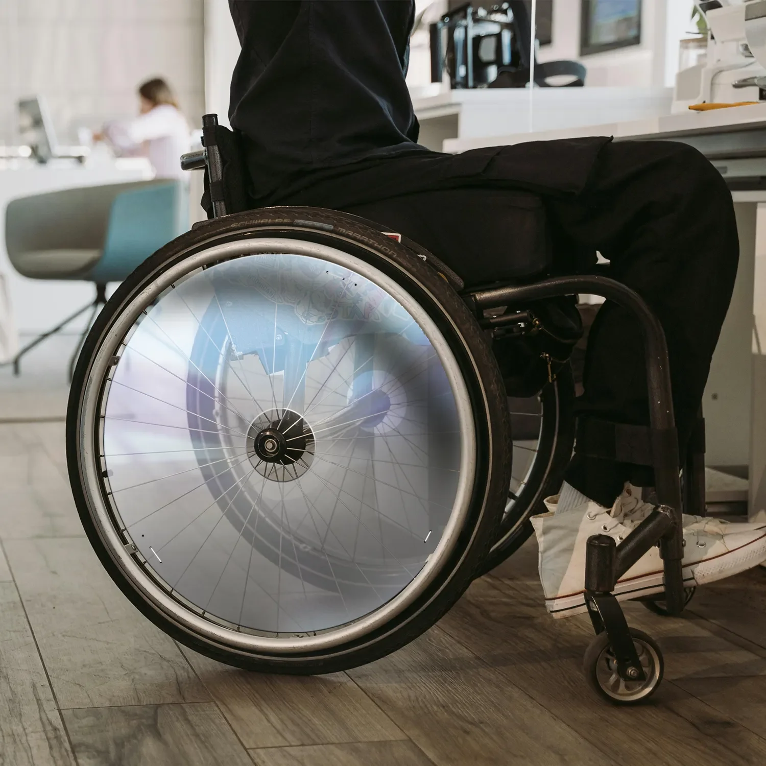 Man using wheelchair with transparent spoke guards in an indoor office setting