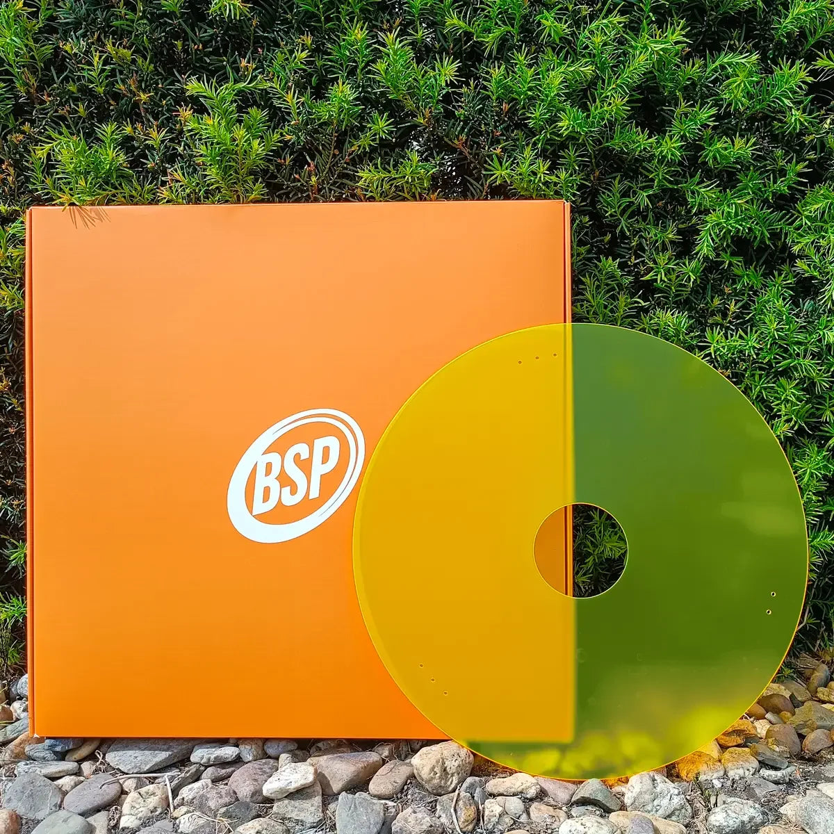 BSP branded orange box with yellow-green circular wheelchair spoke guard on rocks and greenery