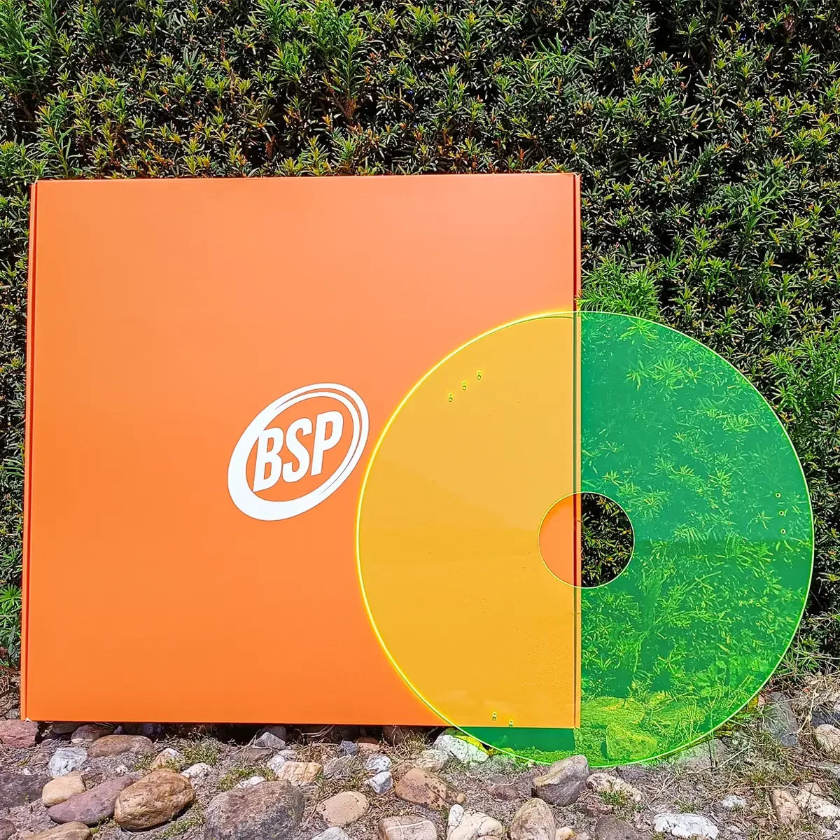 Orange BSP box with yellow-green translucent disc against green foliage, showcasing durable wheelchair accessory packaging.