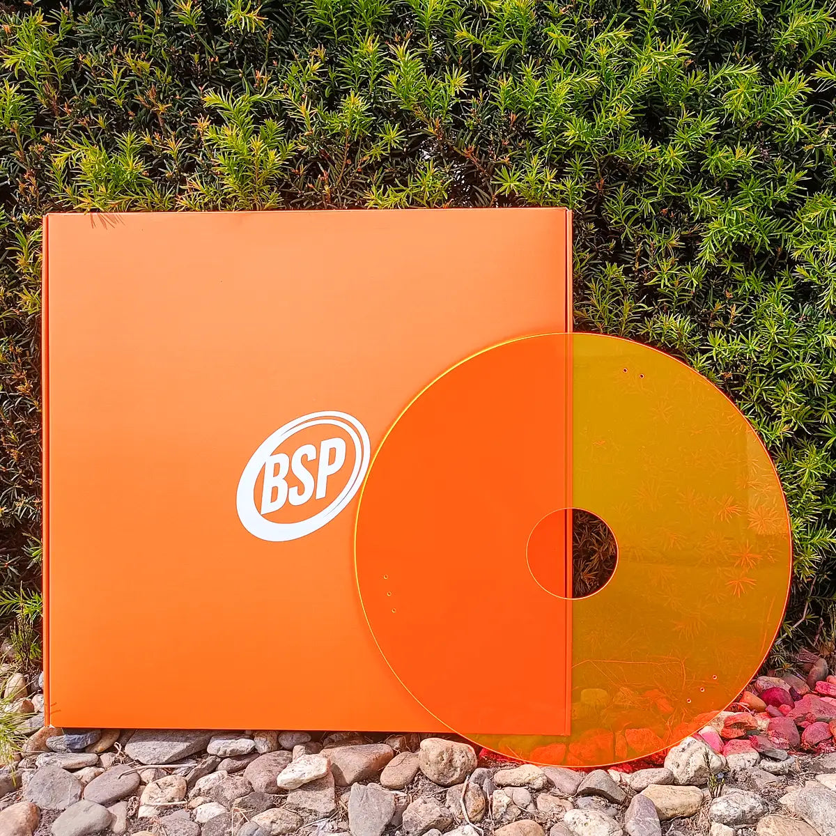 Neon orange wheelchair spoke guards displayed outdoors near a green hedge and rocks.