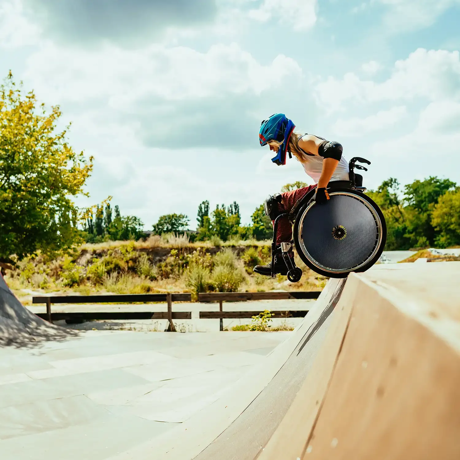 Sport wheelchair user wearing helmet and carbon spoke guards riding at outdoor skatepark