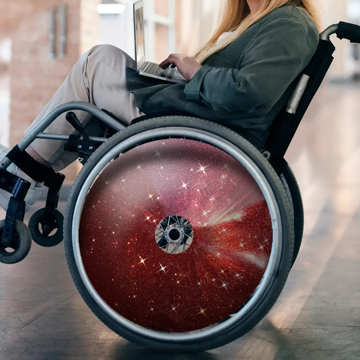 Wheelchair with red galaxy spoke guards, user typing on laptop, durable wheelchair accessory for everyday use