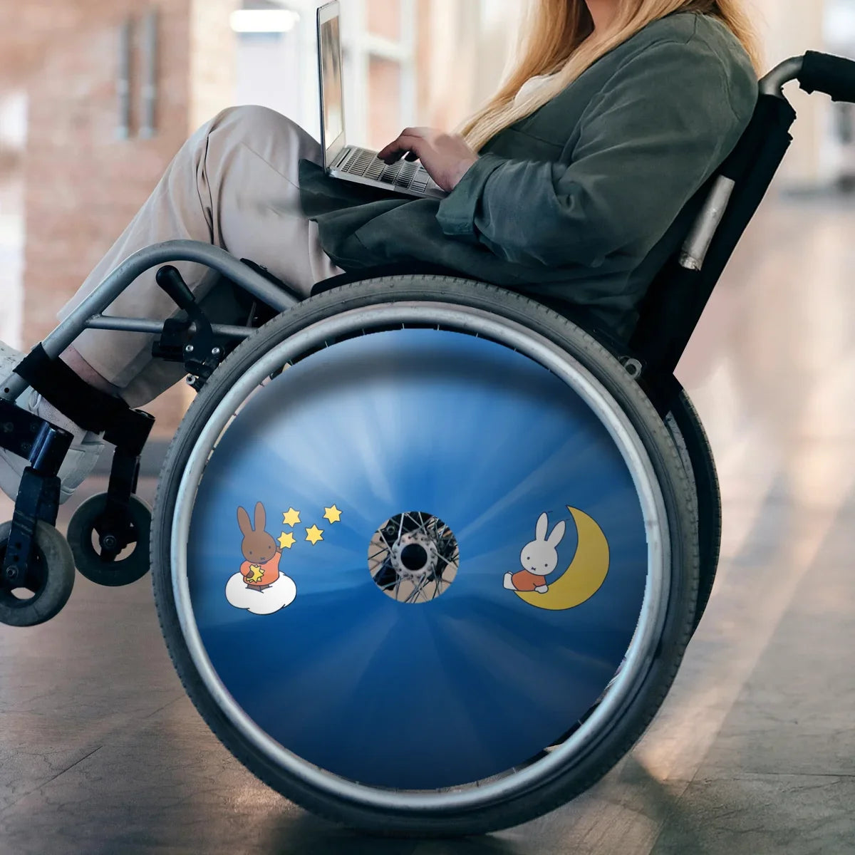 Woman in wheelchair with blue star-themed spoke guard featuring cartoon bunnies, indoors
