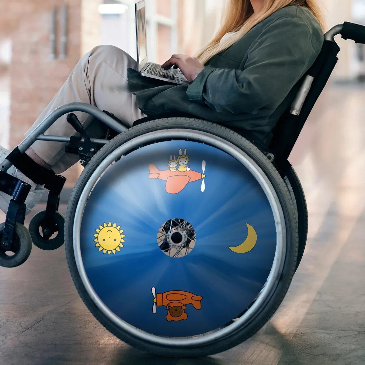 Woman in wheelchair with colorful spoke guard featuring cartoon plane, sun, moon designs