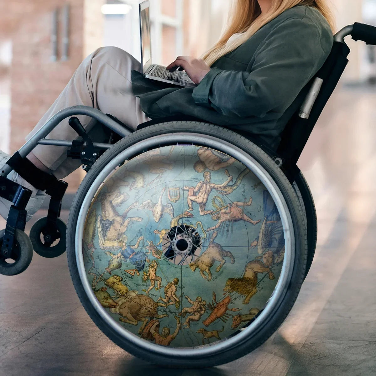 Woman in wheelchair with celestial globe spoke guard design on wheel, using laptop indoors