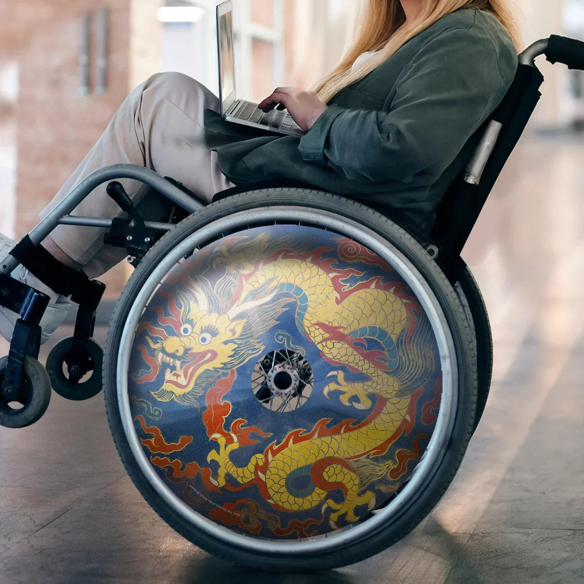 Woman in wheelchair with vibrant dragon spoke guard, using laptop indoors