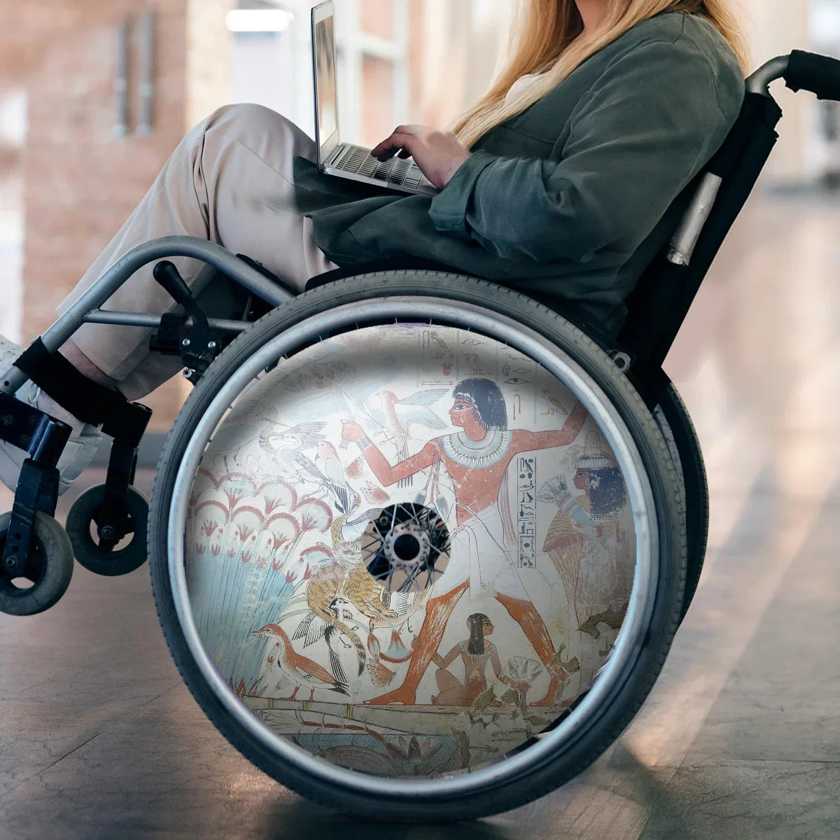 Woman in wheelchair with laptop and Egyptian art spoke guard on wheelchair wheel