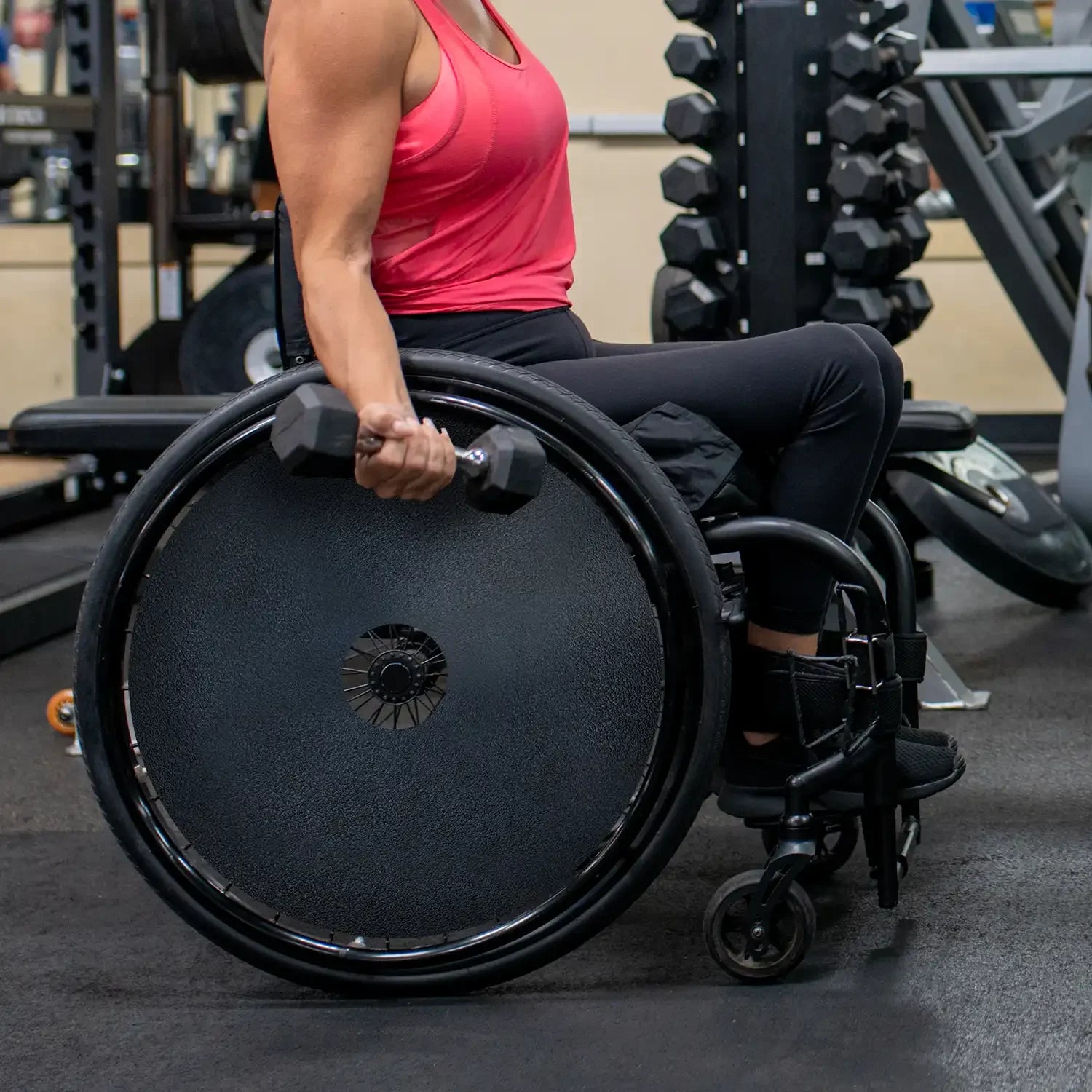 Woman using a wheelchair with spoke guards lifting dumbbell in gym setting
