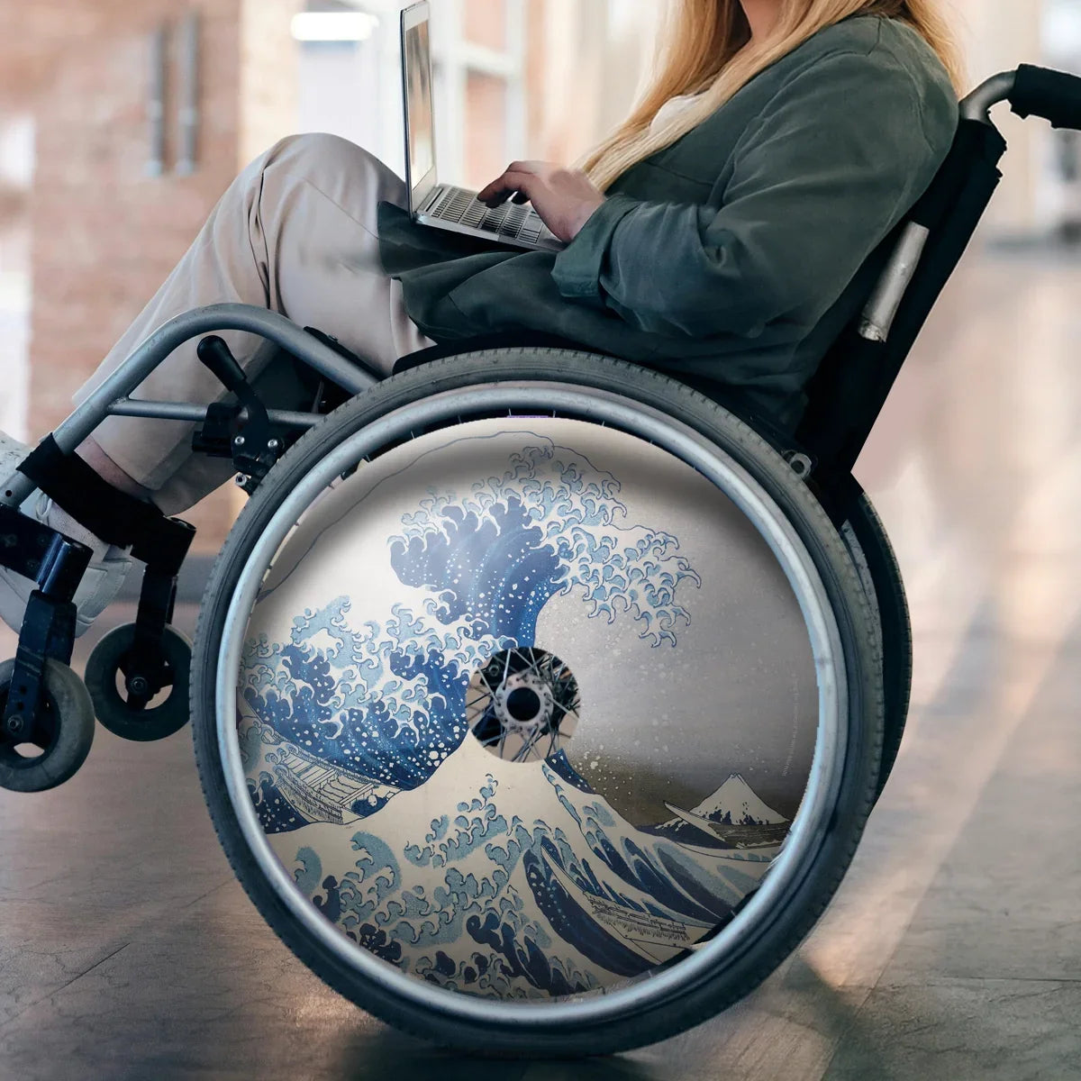 Woman in wheelchair with laptop, wheel features The Great Wave spoke guard design