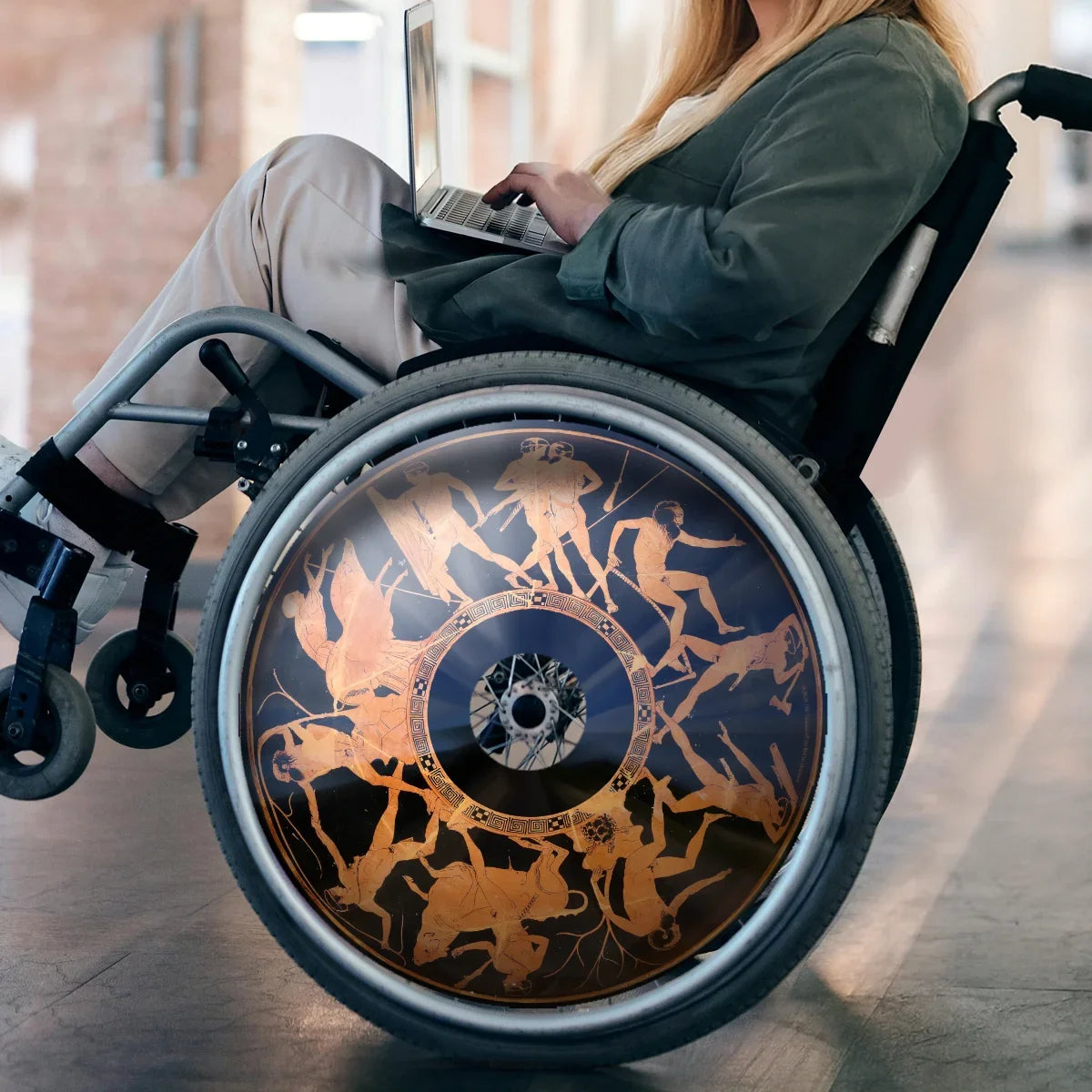 Woman in wheelchair with laptop, featuring Greek mythology Minotaur-themed spoke guard.