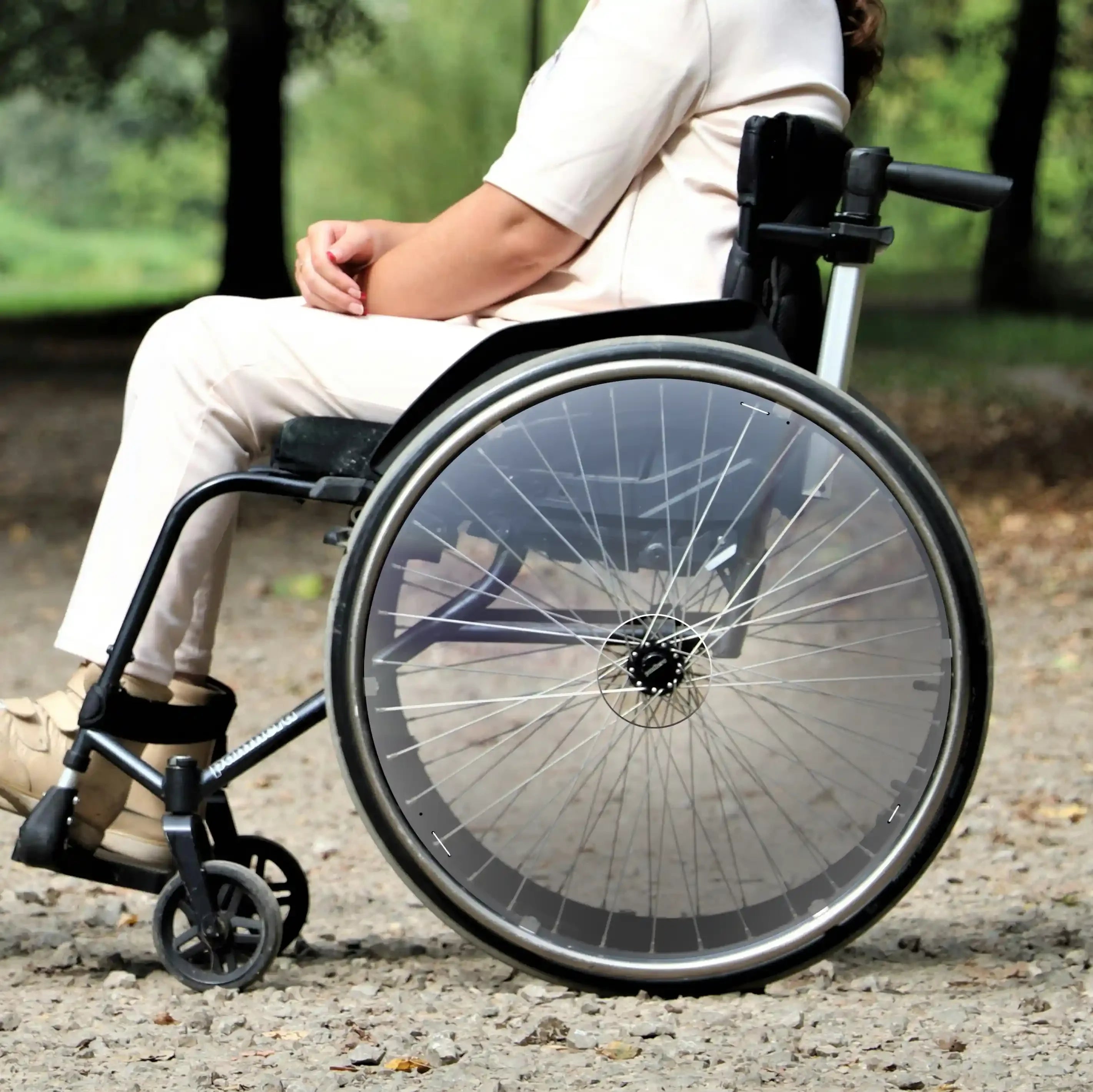 Woman seated outdoors in wheelchair with transparent spoke guards with cutouts