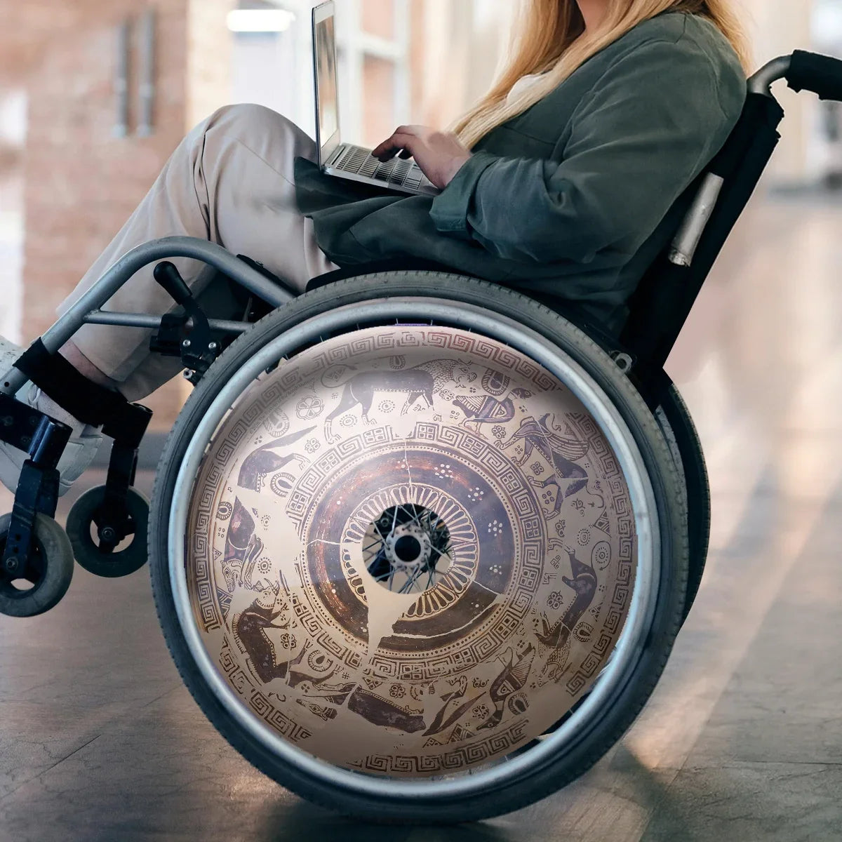 Woman using laptop in wheelchair with decorative wild goat spoke guard in bright hallway